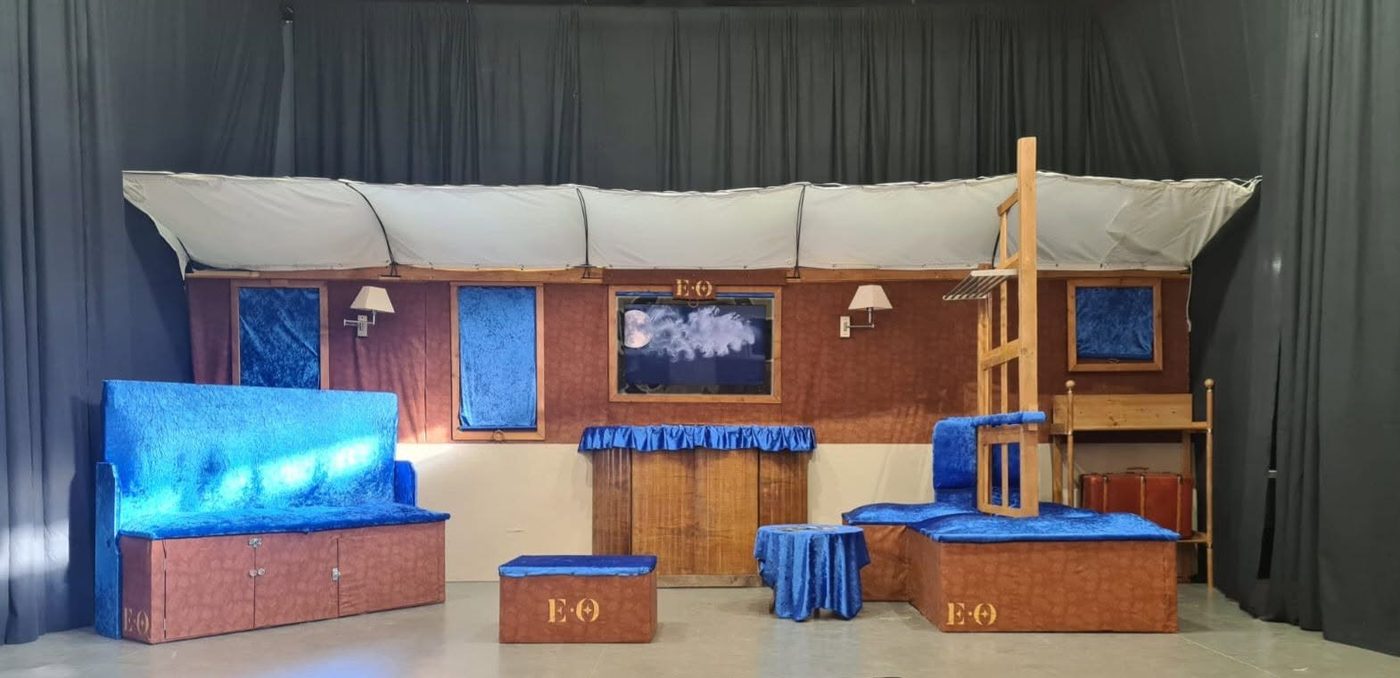 Décor d'un spectacle : un wagon aux banquettes de velours bleu, sur une scène aux rideaux noirs