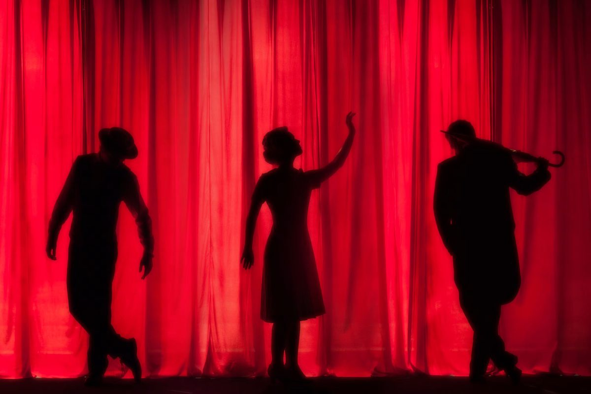 Silhouettes de trois comédiens devant un grand rideau rouge de théâtre